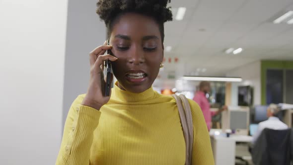 Happy african american businesswoman talking on smartphone and walking in office