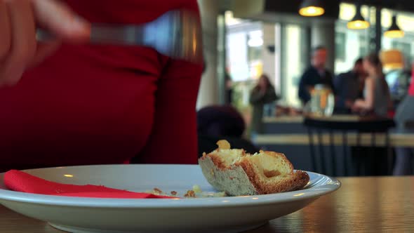 A Woman Sits at a Table in a Cafe and Finished Her Pie, Other Customers in the Blurry Background