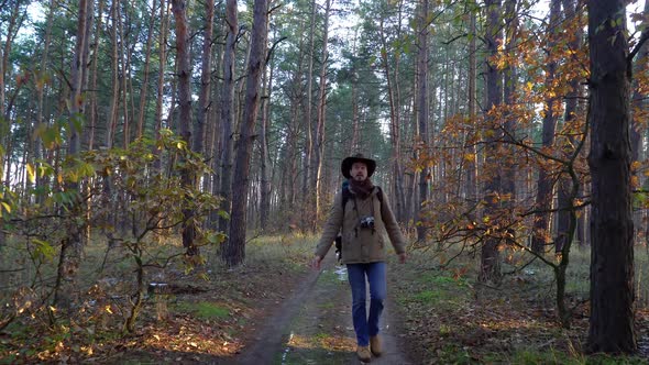 Backpacker with Camera Walks Along a Trail in the Forest