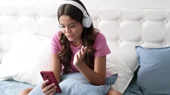 Emotional Kid in Headphones Having Online Conversation Using Cell Phone Blogging