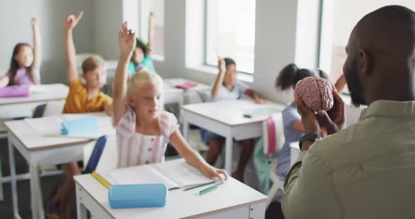 Video of african american male teacher and diverse pupils raising hands during lessons