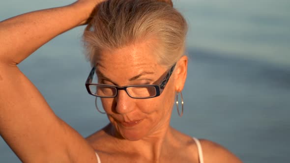 Closeup of mature blonde woman with gray hair playing with her hair and looking old in granny glasse