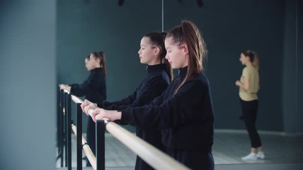 Little Girl Twins Synchronously Stretching By the Stand and Their Trainer Watching Them