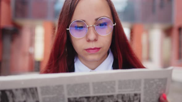 Thoughtful Young Woman Reading Newspaper on Street