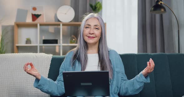 Mature Lady which Sitting on the Soft Couch in Zen Pose and Looking Into Camera