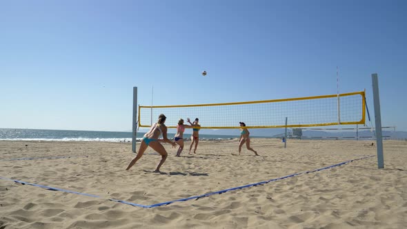 Women players play beach volleyball and a player blocks the ball.