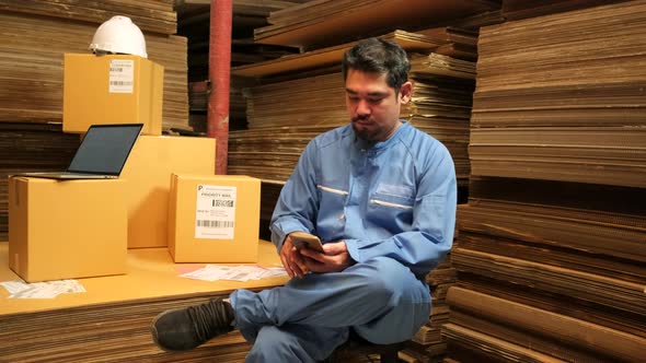Asian male worker mobile phone chat to check orders at parcels warehouse.