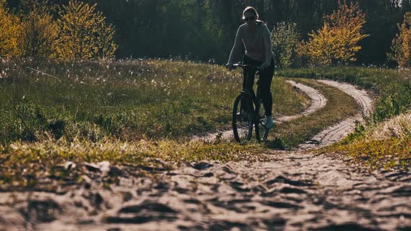 Young Woman on a Bicycle Rides Along Green Forest Path in Sunny Summer Day