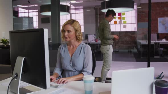 Caucasian businesswoman working on laptop with mixed race colleague in background using memo notes