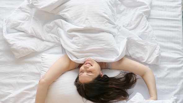 Young Happy Woman Wakes Up Stretching Arms on Bed at Home