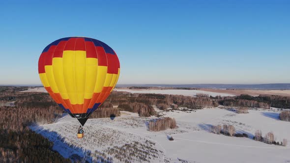Aerial Shot of the People Fly on a Big Bright Balloon Over the Winter Forest alt
