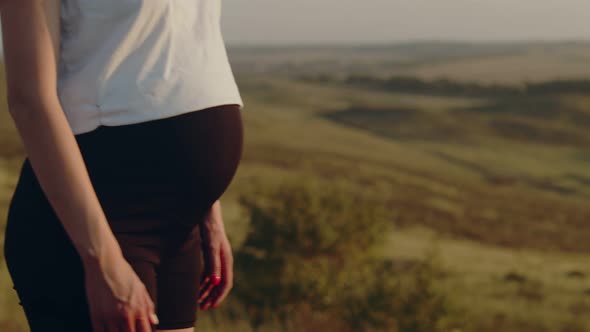 Pregnant Young Woman Prays with Her Hands Clasped Together Outdoor on Top of Hill Side View