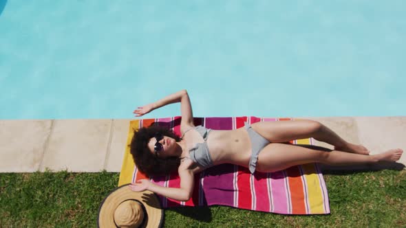 Mixed race woman lying on blanket sunbathing by the pool