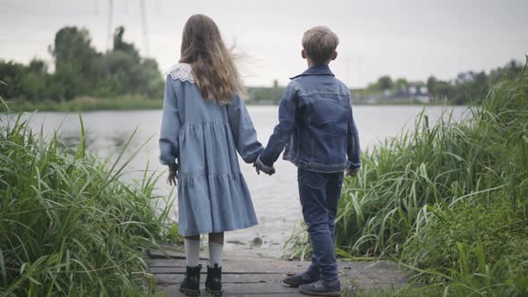 Wide Shot of Loving Schoolchildren Standing on River Bank Holding Hands