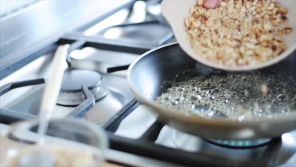 Woman putting chopped nuts in pan on stovetop