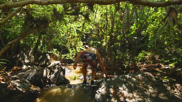 SLOWMO, Young man explores a tropical jungle, ducking under branches and walking through a stream at