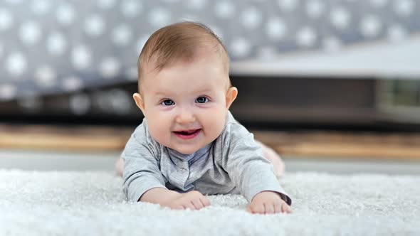 Portrait of Little Smiling Toddler Lying on Fluffy Carpet Looking at Camera in Modern Interior