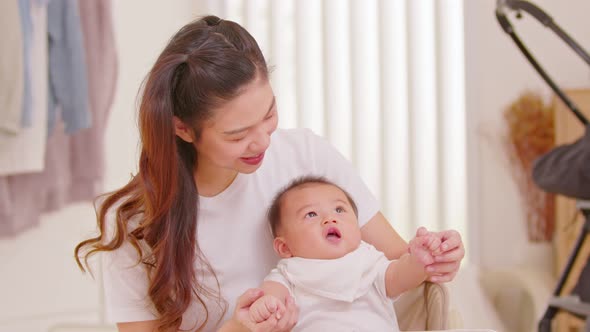 New asian mom playing to adorable newborn baby on chair smiling and happiness at home.Happy Mother t