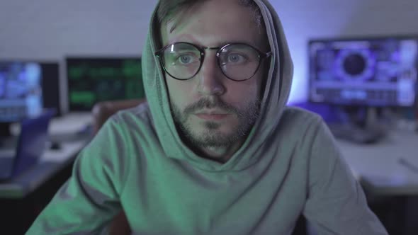 Close-up of Concentrated Man in Eyeglasses Looking at Camera with Multiple Computers at the