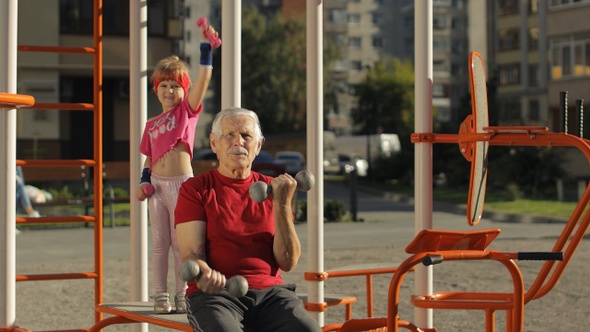 Granddaughter and Grandfather Doing Fitness Exercises with Dumbbells. Senior Man with Child Kid Girl