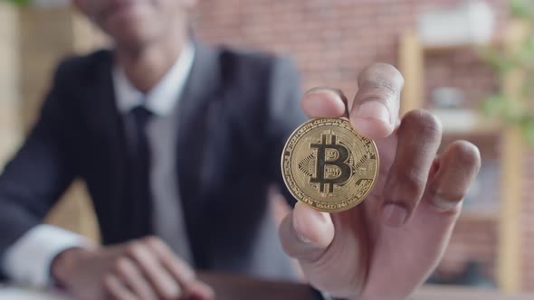 Close-up of gold bitcoin coin in the hand of a black corporate businessman man in a suit the office.