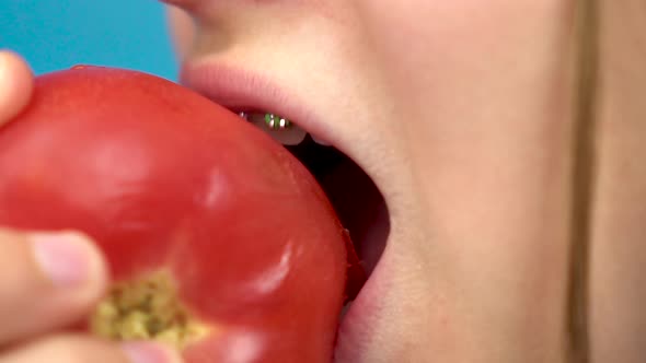 Teenage Girl with Braces on Her Teeth Eats a Red Tomato on a Blue Background. Girl with Colored