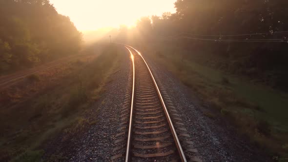 Slow flight of a drone over a foggy railway passing through the autumn forest at dawn