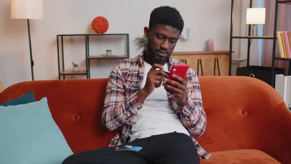 Man Sitting at Home Using Credit Bank Card and Smartphone While Transferring Money Online Shopping