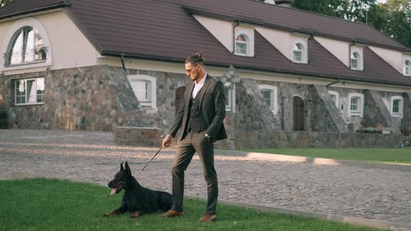 A Rich Businessman in a Business Suit Walks with a Large Doberman in the Park. Successful Bearded