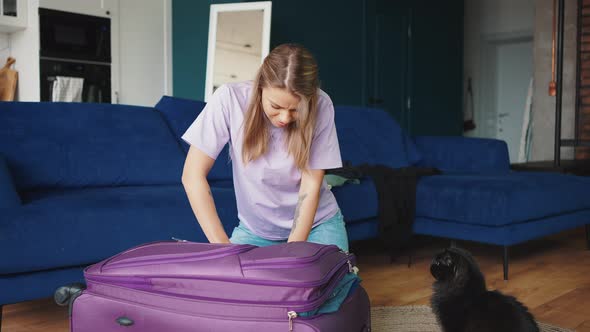 Young Blonde Woman Packing Luggage for Vacation Trying to Close Suitcase with Too Many Clothes