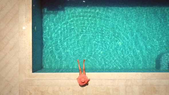 Aerial view of female with hat sitting by swimming pool.