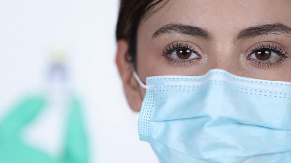 Rack focus from eyes of woman wearing mask to vaccine vial