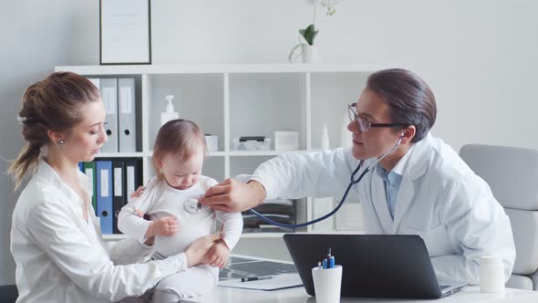 Male pediatrician is examining little baby. Doctor, mother and daughter in medical office.