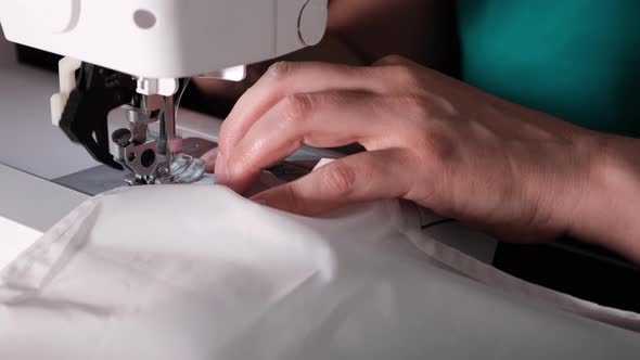 A hand of a young seamstress sewing a white cloth tailoring according to the tradition of tailors.