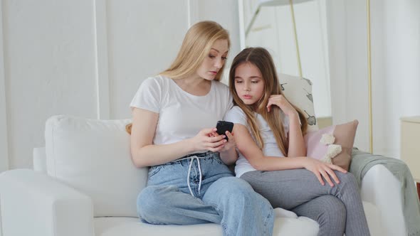 Concentrated Adult Mother and Teenage Daughter Child Girl Sitting at Home Couch Looking at Mobile