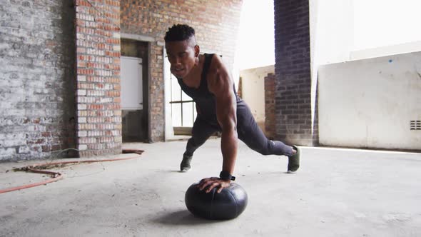African american man exercising doing push ups on medicine ball in an empty urban building