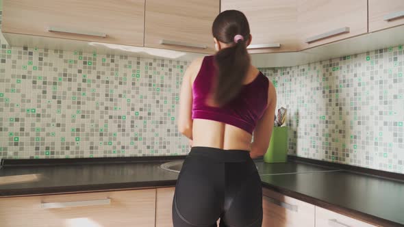 Beautiful slender young girl in headphones dancing and washing dishes in the kitchen in the sink.