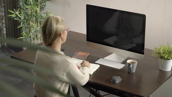 Woman Looking at Monitor's Computer Listening Conference Lesson Writing and Taking Notes