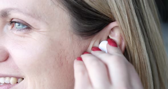 Smiling Beautiful Woman Inserts Wireless Headphones Into Ear Closeup