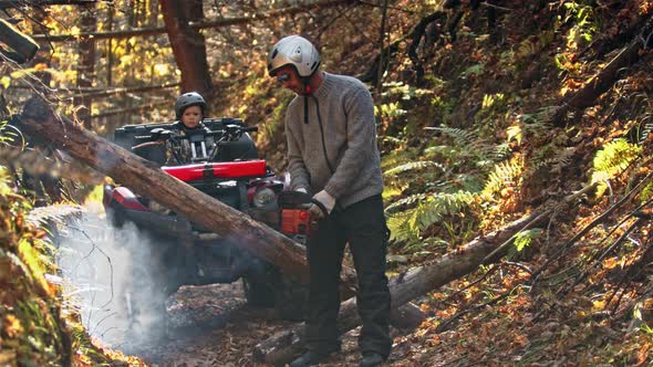 A Man Turns on a Chainsaw in the Forest and His Son Is Waiting for Him on a Quad Bike