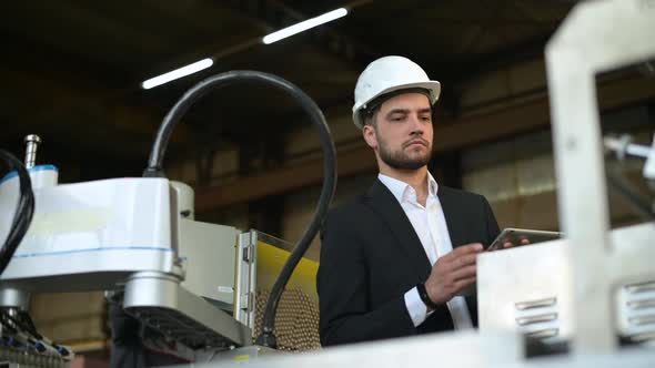 A young plant manager controls the machine's process and takes notes on a tablet