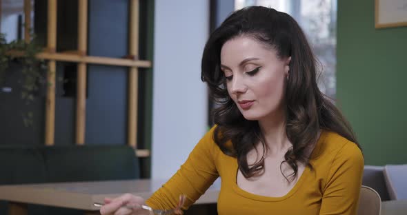 Gorgeous Brunette Caucasian Young Woman Smelling and Eating Delicious Pizza in Restaurant