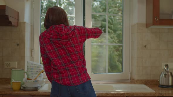 30s Woman Opening Window to Enjoy Fresh Air Standing in the Kitchen