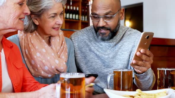 Friends looking their photos on mobile phone in bar 4k