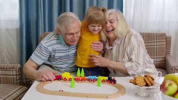 Child Girl Kid Involved in Build Board Game Ride Toy Train on Railroad with Senior Grandparents Home
