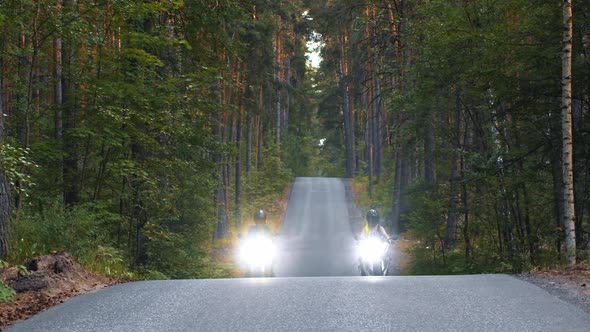 Motor Riding Two Women in Helmets Riding Motorcycles on Empty Road in the Woods with Turned on