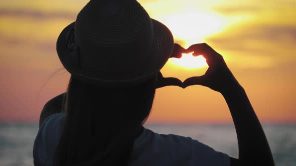 Young Beautiful Girl Makes Heart By Her Hands in Heart Shape Framing Setting Sun at Sunset Over