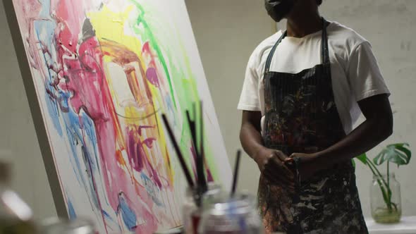 African american male artist wearing face mask tying his apron at art studio
