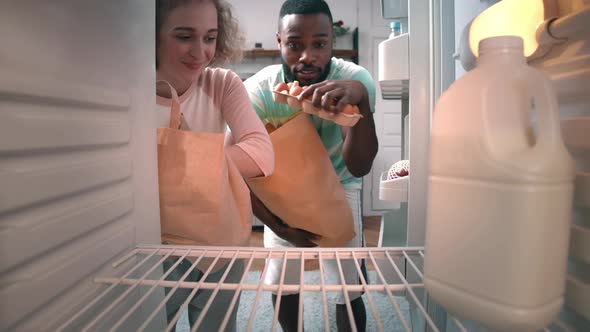 Multiethnic Couple Unpacking Groceries in Fridge at Home