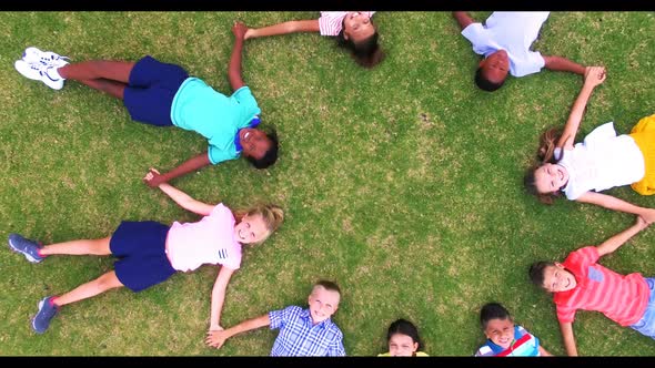 School kids holding hands while lying in circle on grass